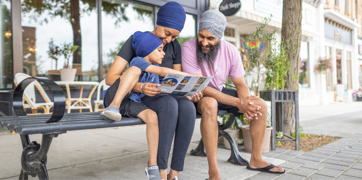 A mother, child, and father are sitting on a bench looking at a brochure.